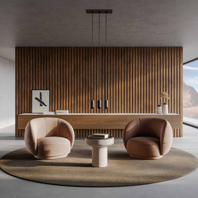 Seating area with two tan armchairs on a circular brown carpet. Wood panel wall in the back, with a large console in front. A Tivoli table in the center of the room between the two chairs with books on it. The console has two Tivoli vases in Travertino Navona marble with Black Emperador top on right side. Large size (right) with brown, dried hydrangea flowers and and Small size (left).  A long black light fixture with 3 long strands that hangs down .