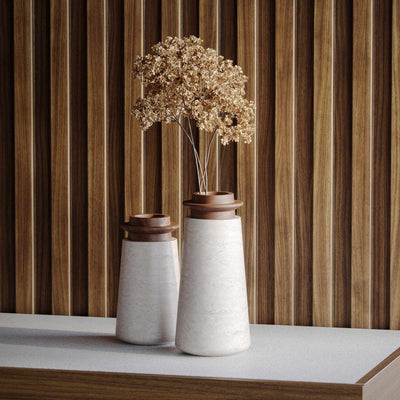 Two Tivoli vases in Travertino Navona marble with Walnut wood top. Large size (right) with brown, dried hydrangea flowers and and Small size (left). On a white countertop with wood paneled wall behind. 
