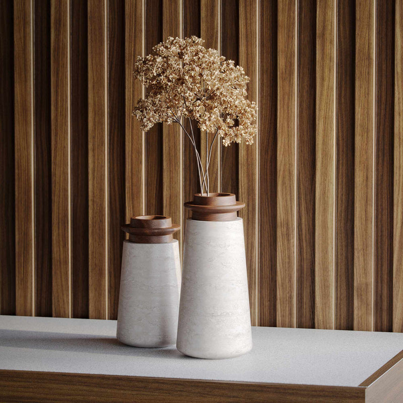 Two Tivoli vases in Travertino Navona marble with Walnut wood top. Large size (right) with brown, dried hydrangea flowers and and Small size (left). On a white countertop with wood paneled wall behind. 