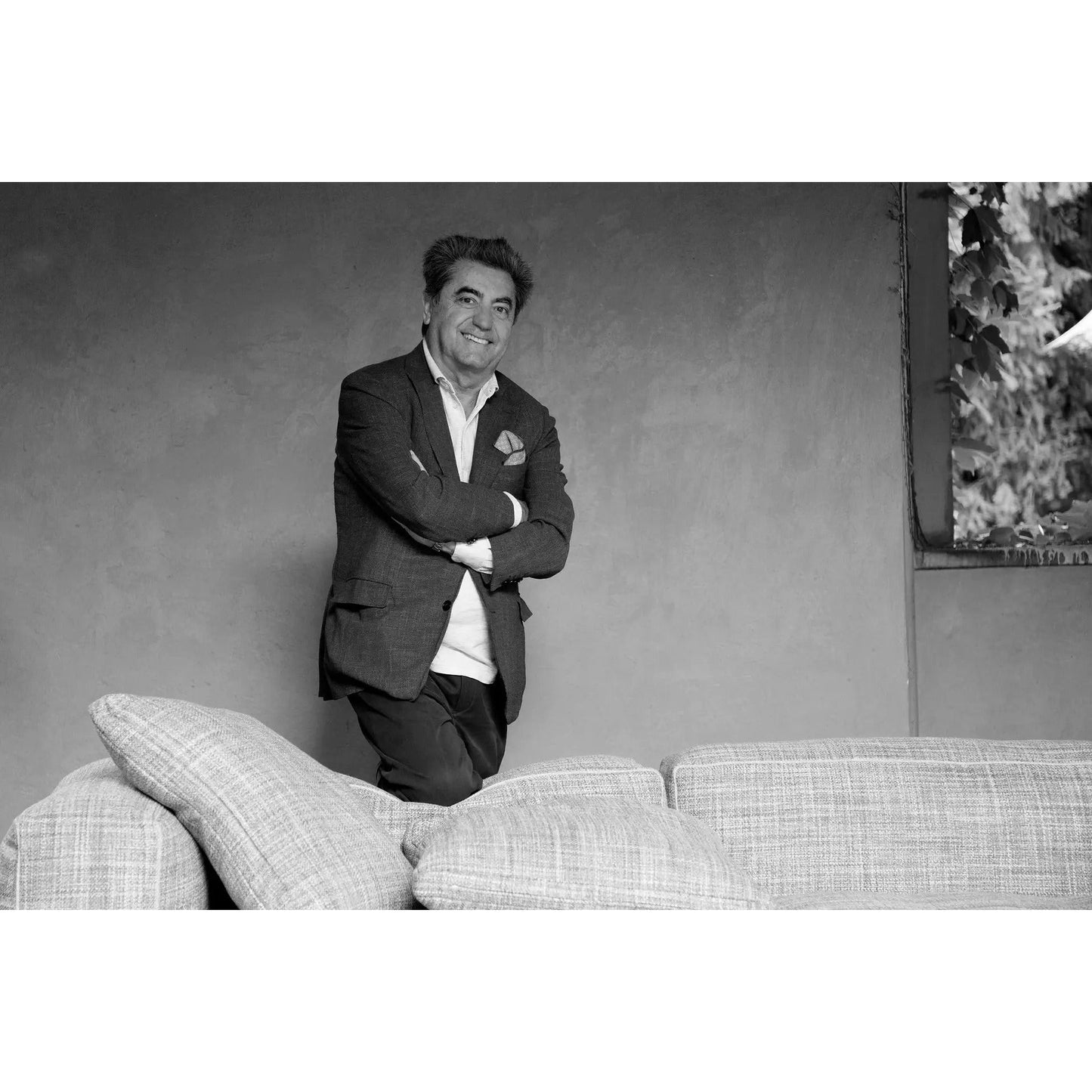 Portrait of Antonio Citterio, the acclaimed designer of the B&B Italia Richard Bed, standing behind a modern sofa.