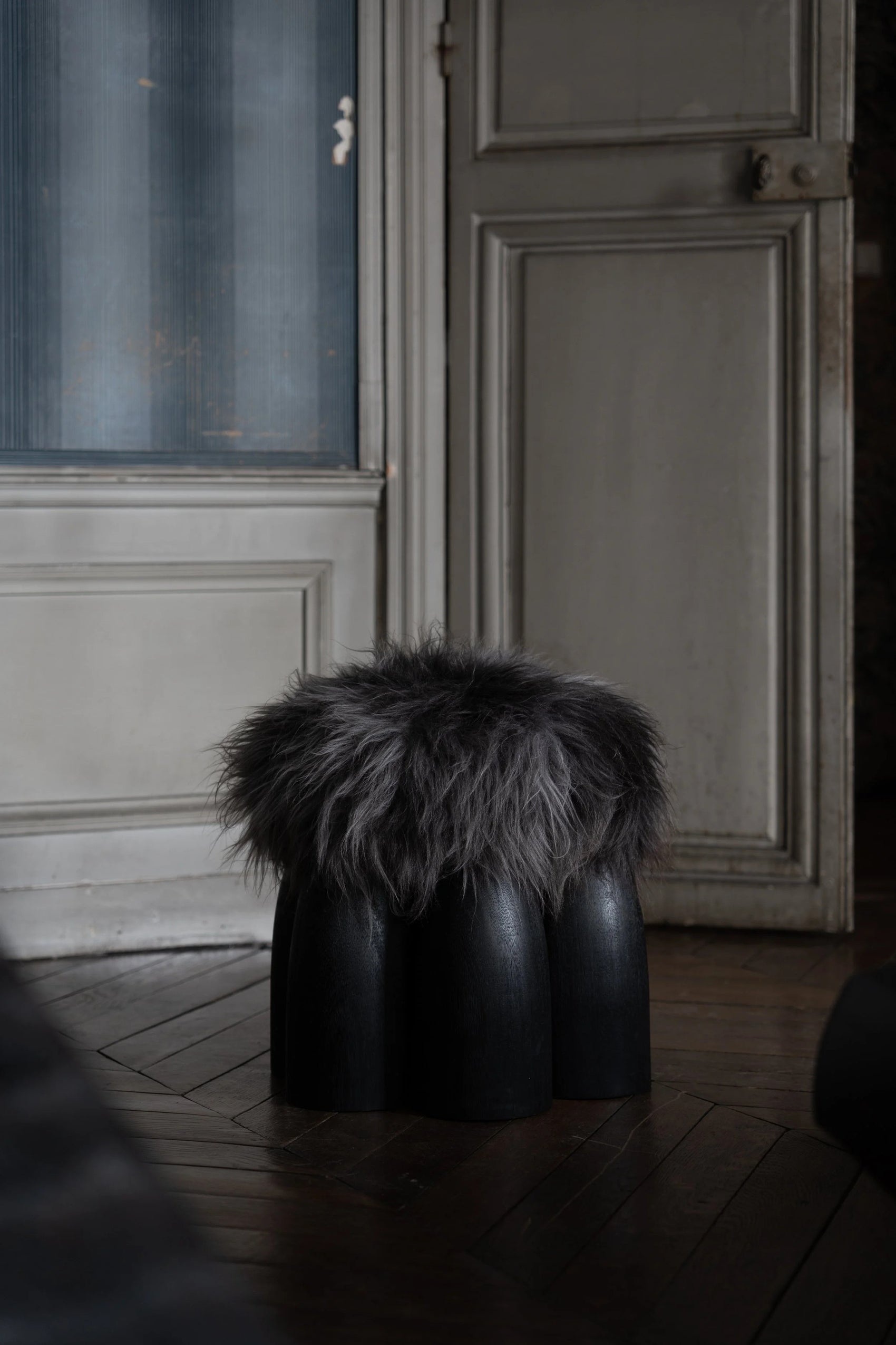 Senufo Ottoman by Arno DeClercq with Black African Walnut base and Sheep Wool seat in an elegant interior setting.