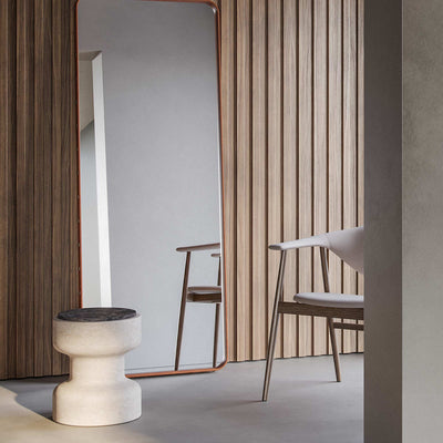 Tivoli stool in Travertino Navona base and Black Emperador (bottom left). In a room with a mirror and a chair with wood paneled wall in background.