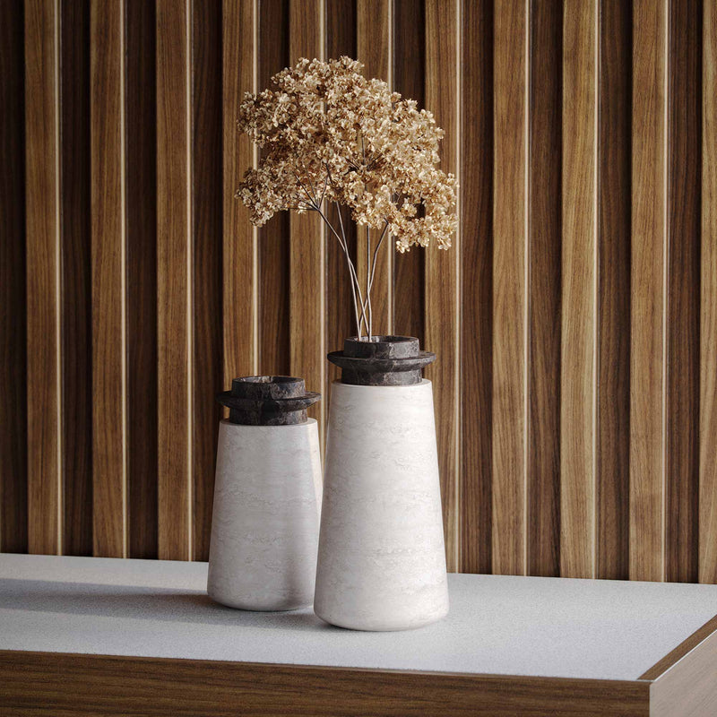 Two Tivoli vases in Travertino Navona marble with Black Emperador top. Large size (right) with brown, dried hydrangea flowers and and Small size (left). On a white countertop with wood paneled wall behind. 