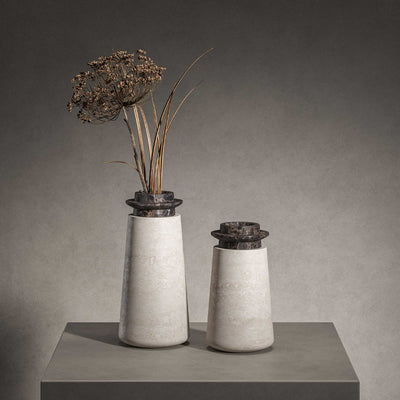 Two Tivoli vases in Travertino Navona marble with Black Emperador top. Large size (left) and Small size (right) with gray background on a gray tabletop. Large vase has dried flowers in it.