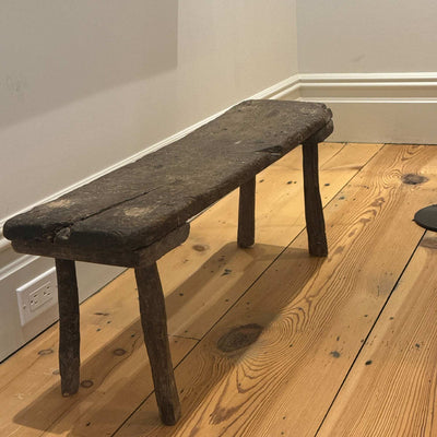 Antique small table made of dark brown wood in a room with white background and hardwood floors