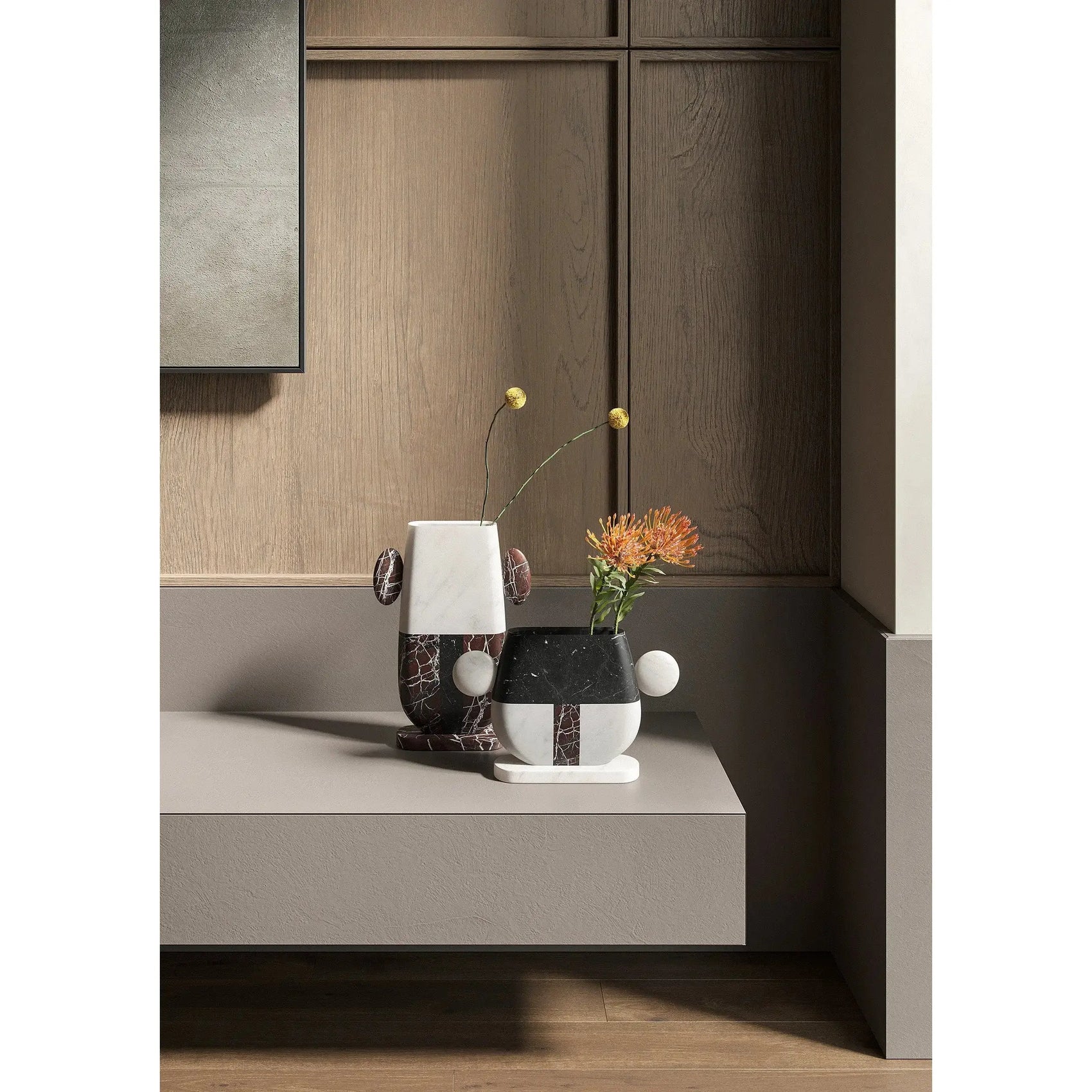 Two artistic Pietro vases in black and white marble with slender floral arrangements on a modern table against wood paneling