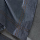 Close-up detail of Society Limonta Nim bed sheet showing the soft denim-effect cotton weave and contrasting orange stitching.