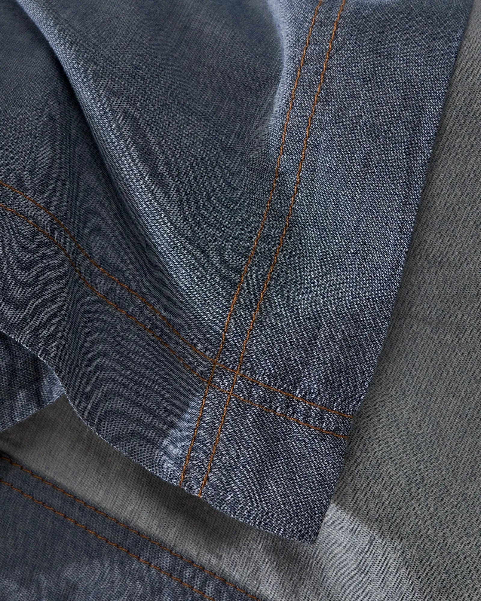 Close-up detail of Society Limonta Nim bed sheet showing the soft denim-effect cotton weave and contrasting orange stitching.